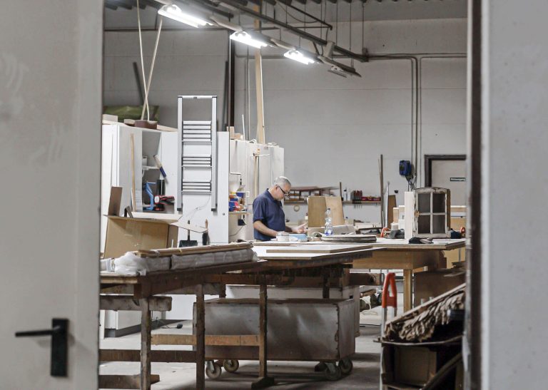 A man measures wood pieces in a wood shop.