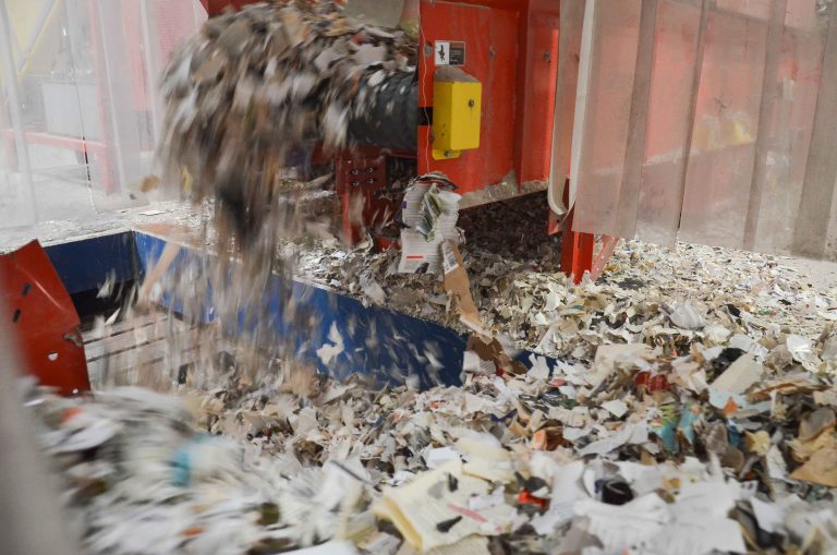 Shredded newspapers fall from the machine onto the conveyor belt.