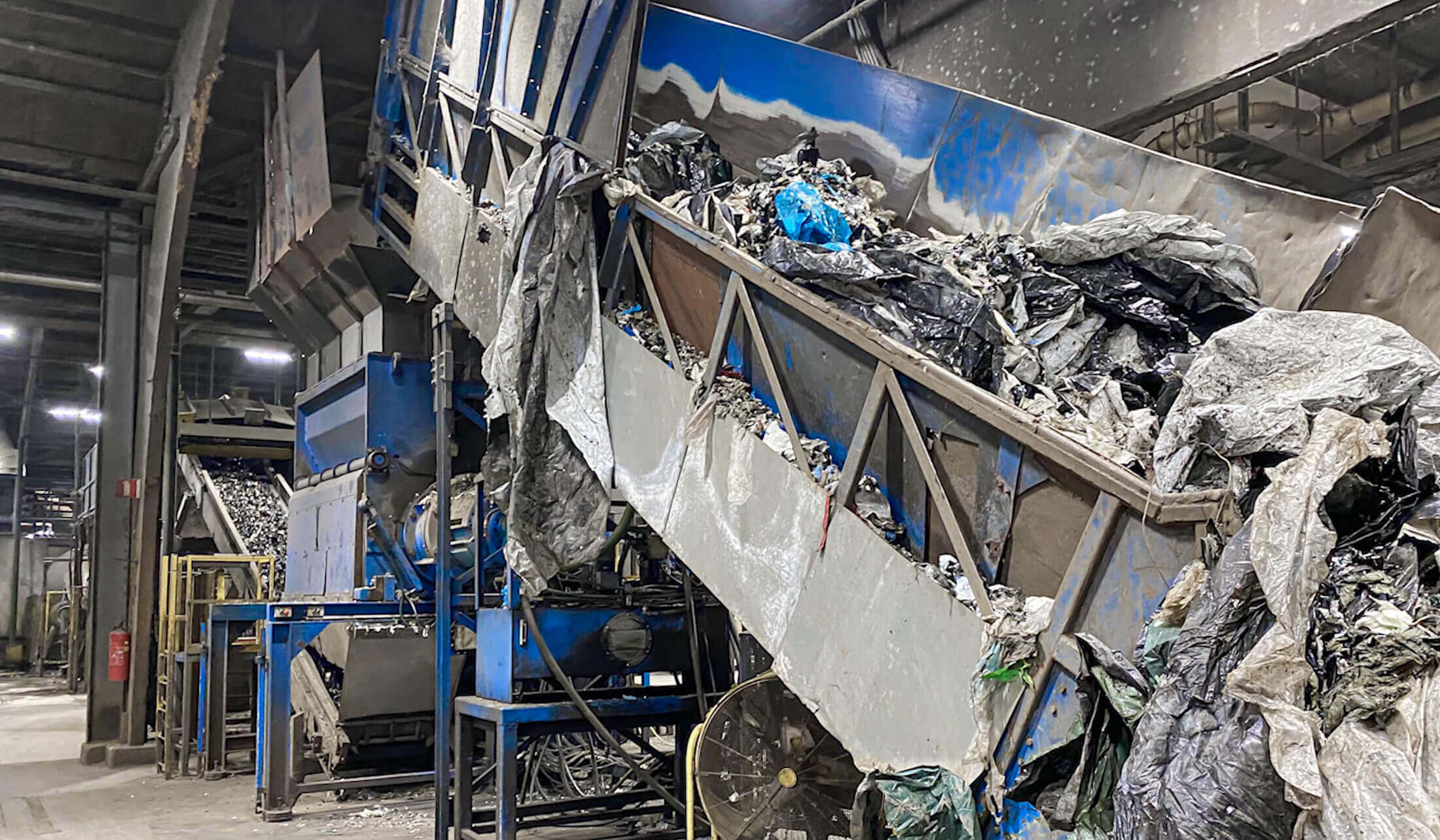 Verunreinigte Landwirtschaftsfolie wird mithilfe eines Förderbands in den Shredder transportiert