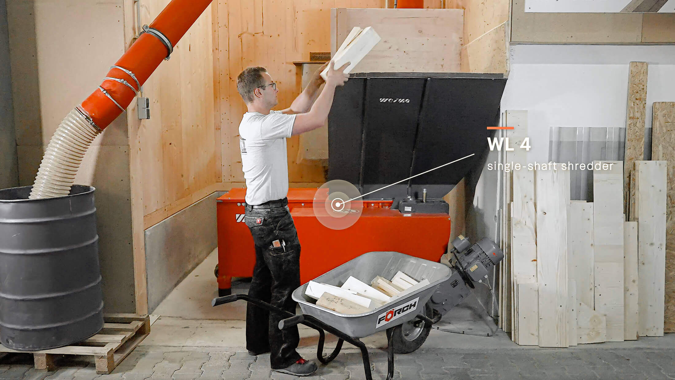 Ein Zimmermann befüllt einen orangenen Holzzerkleinerer von WEIMA händisch mit Holzresten