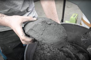 Hand hält Bruchstück von getrocknetem Schleifschlamm über einem Metallfass