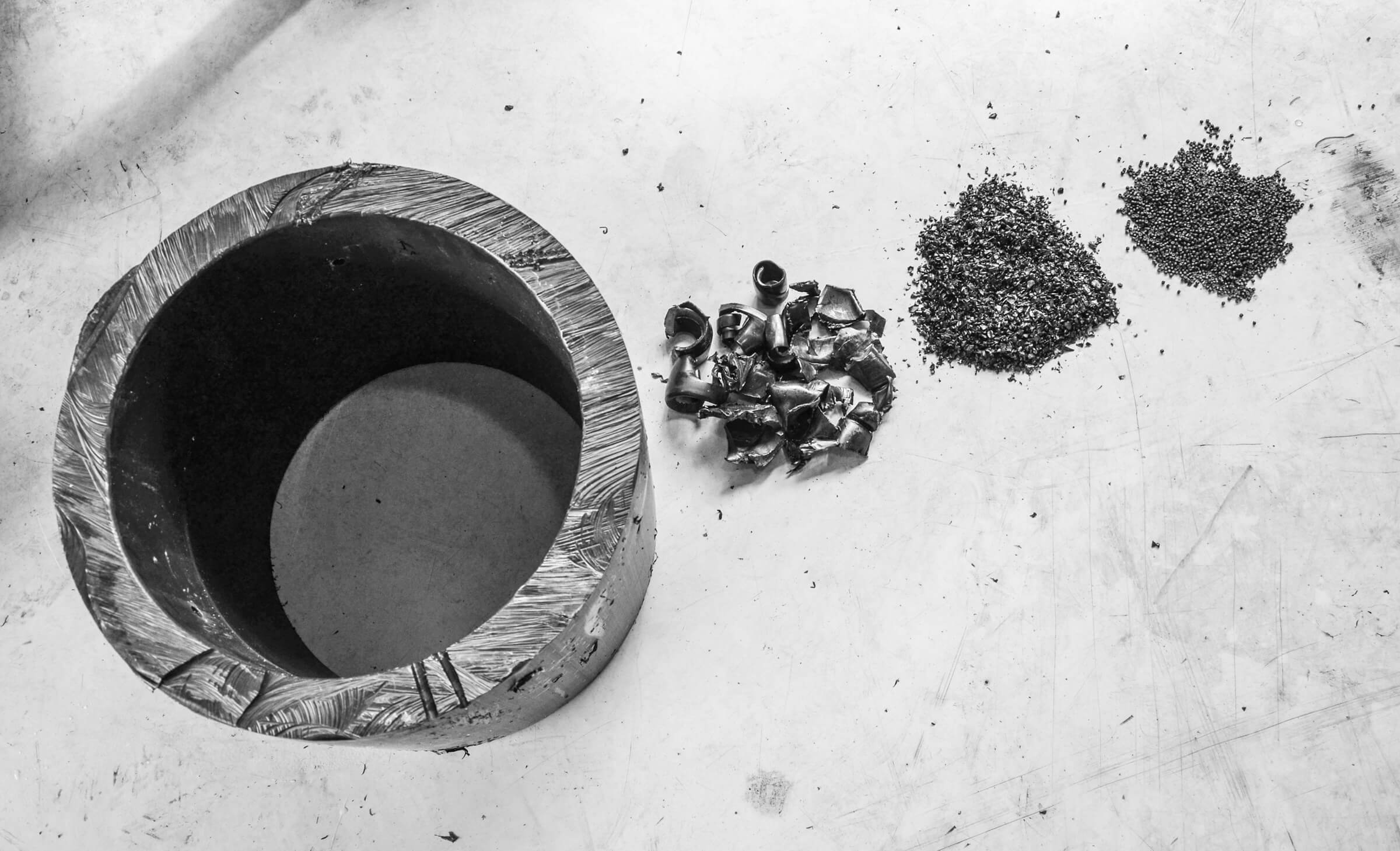 Ein großes schwarzes Kunsstoffrohr neben zerkleinerten und extrudierten Material davon.