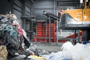 Ein orangener Shredder in Südkorea der alte Textilien zerkleinert die im Vordergrund liegen.