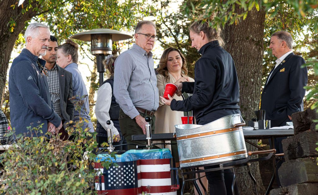 A bartender pours local beer into a cup for an attendee. Other attendees wait in line.
