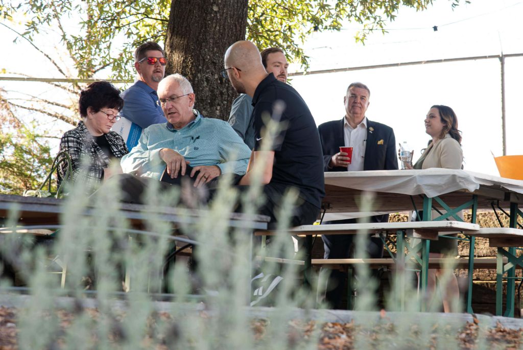 A group of people networks under a large tree, holding cups.