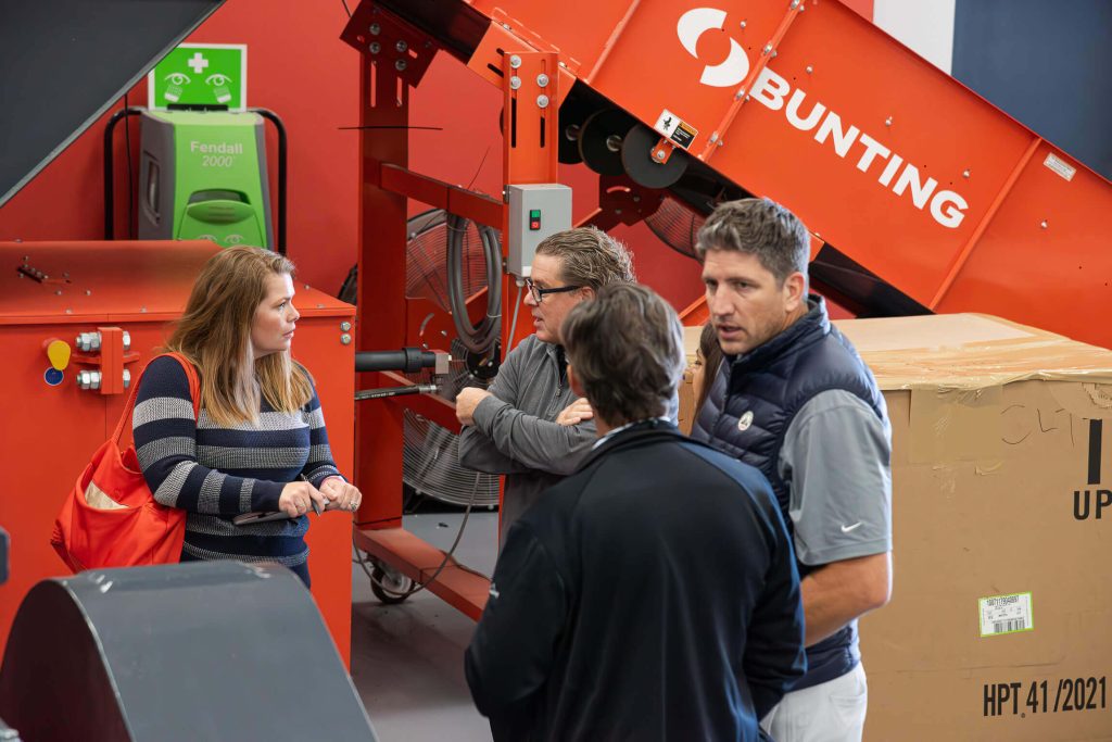 A group of people stand in front of a conveyor while having a discussion.