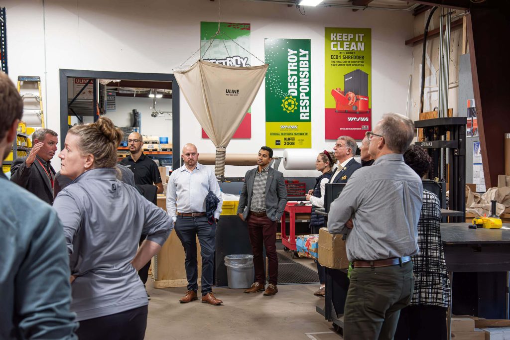 A group of people gather in the parts department and listen to Madison Burt speak.