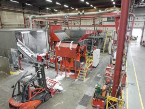 Blick von oben in eine Industriehalle, in der Mitte steht ein orange-roter Shredder, im Vordergrund sieht man einen Gabelstapler