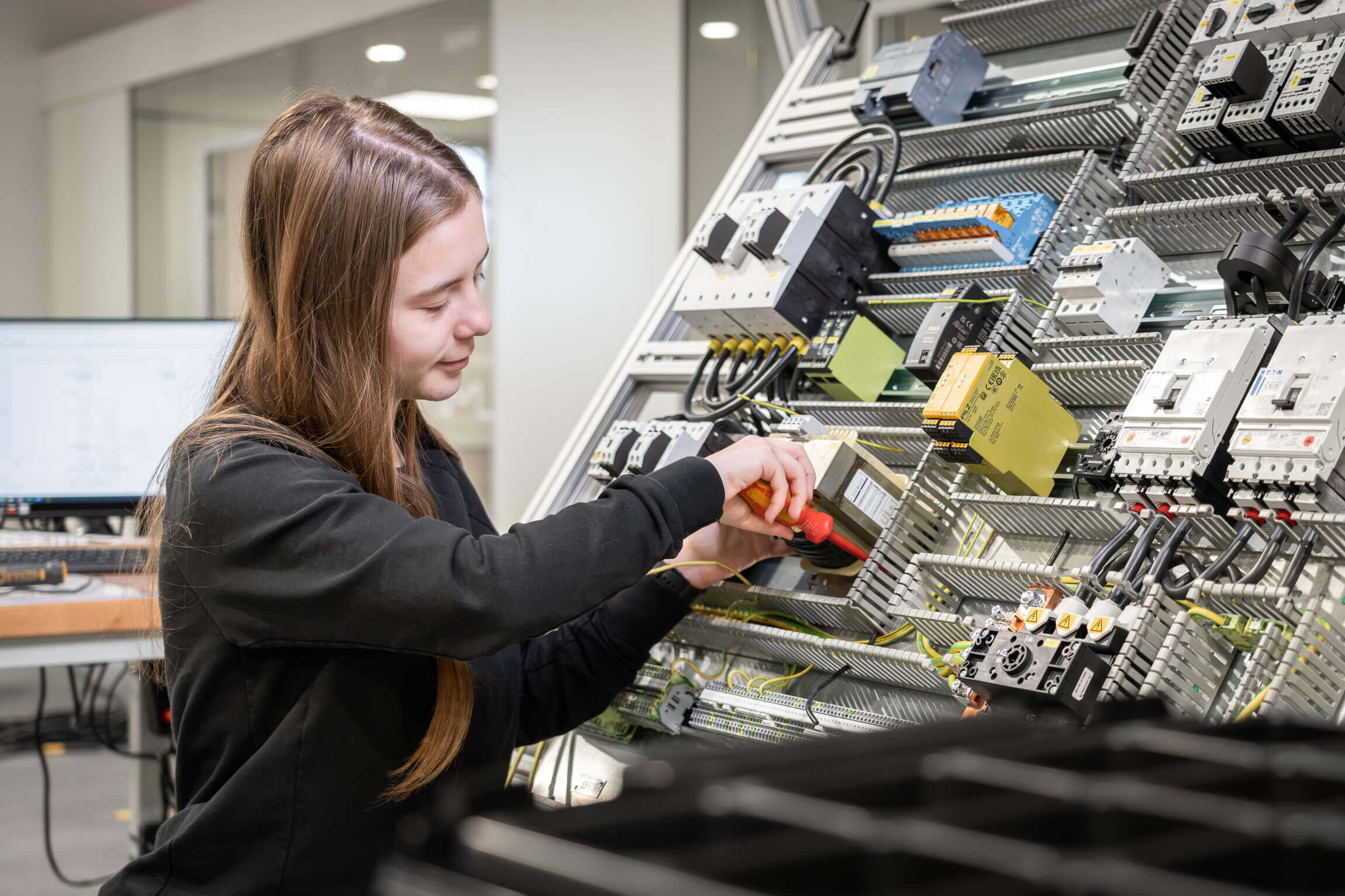 Eine Mitarbeiterin von WEIMA baut und verdrahtet einen Schaltschrank, sitzt davor mit Werkzeug