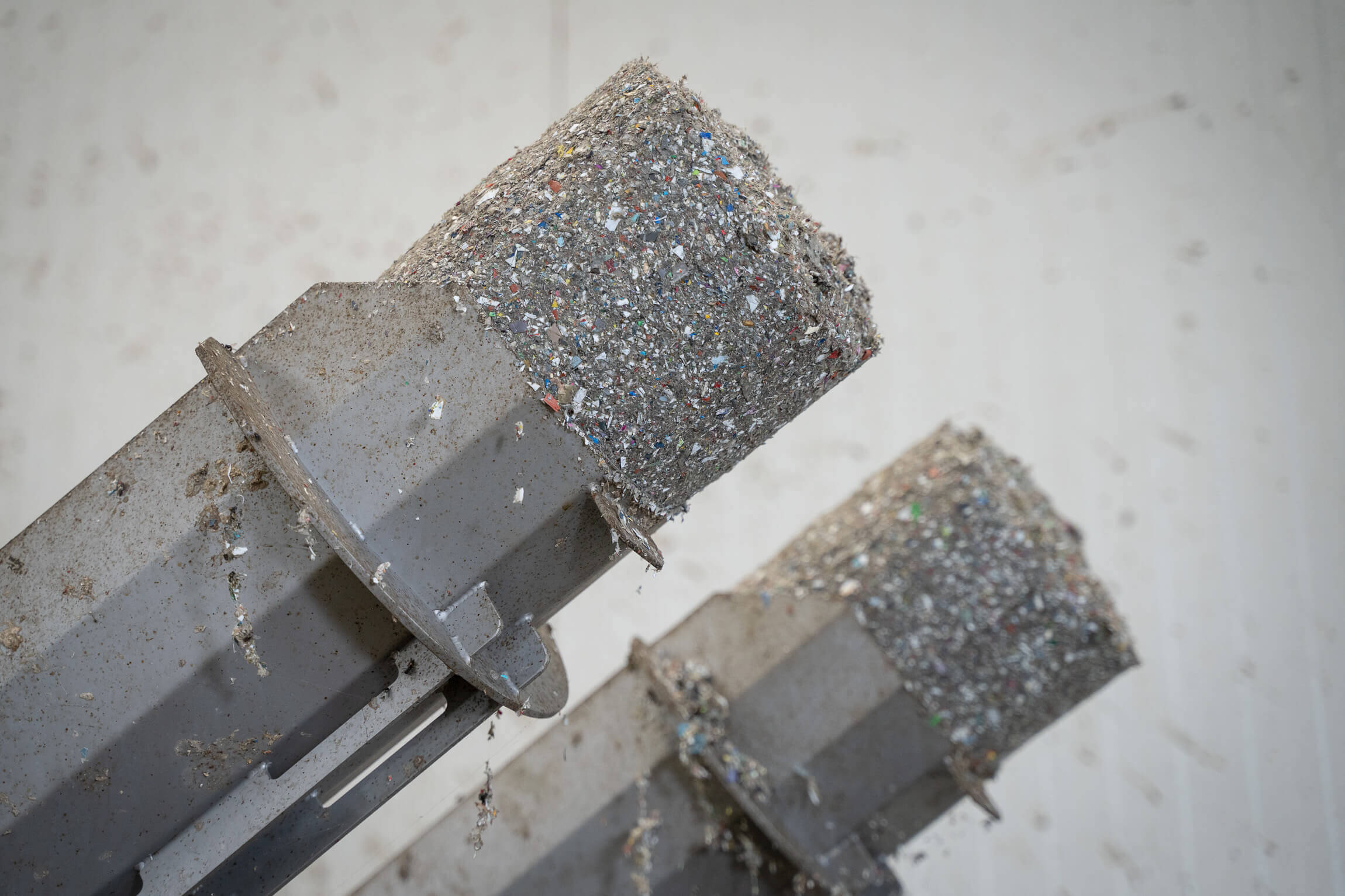 Entwässerte und komprimierte graue Klumpen aus Kunststoff Feinanteilen auf den Austragsrohren einer WEIMA C.200 Duo