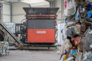 An orange shredder in an industrial hall with post-consumer waste in the foreground