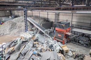EBS Shredder von WEIMA mit Förderband in einer großen Halle, davor ein Berg Abfall