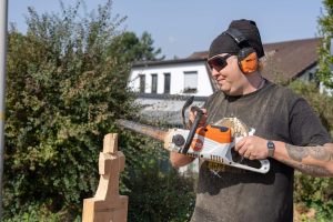Ein Mann schnitzt mit einer Motorsäge eine Figur aus einem Holzblock