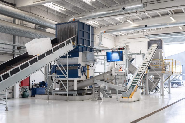 Mehrere IBC Container werden in den WEIMA Shredder befördert, im Hintergrund der Halle ein Granulator und eine Friktionswaschanalage