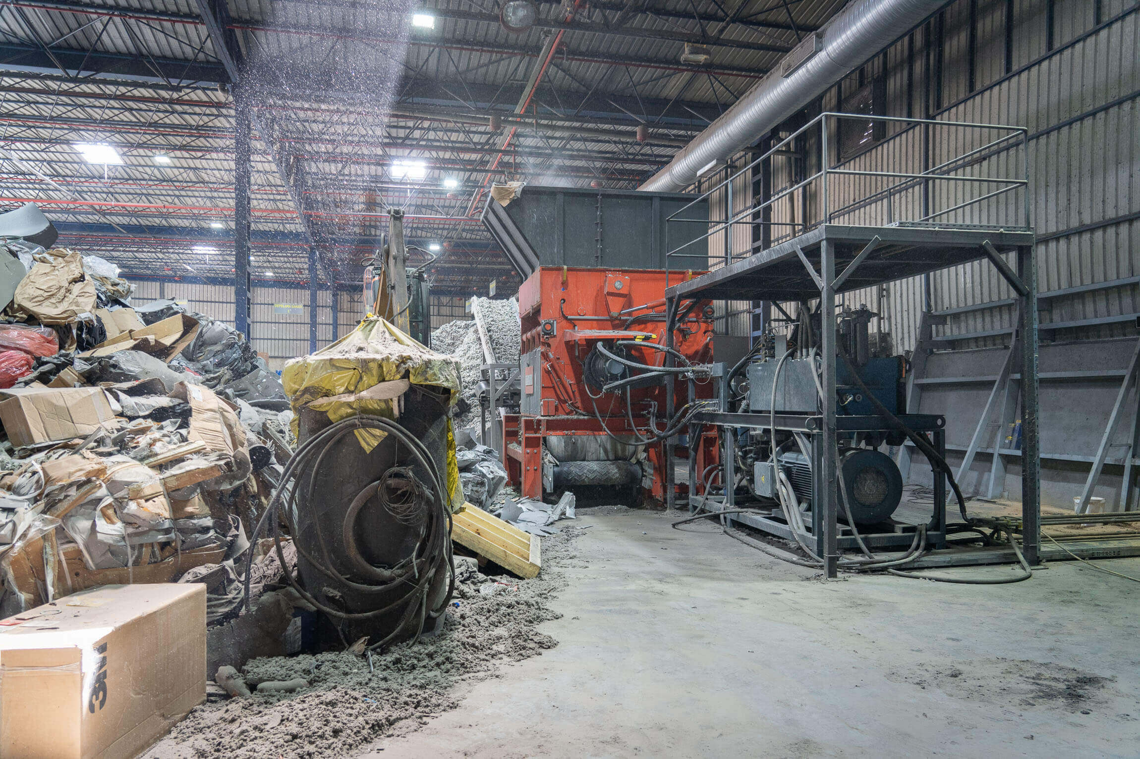 Ein WEIMA Shredder steht in einer Industriehalle, davor der Hydraulikantrieb und Industriemüll