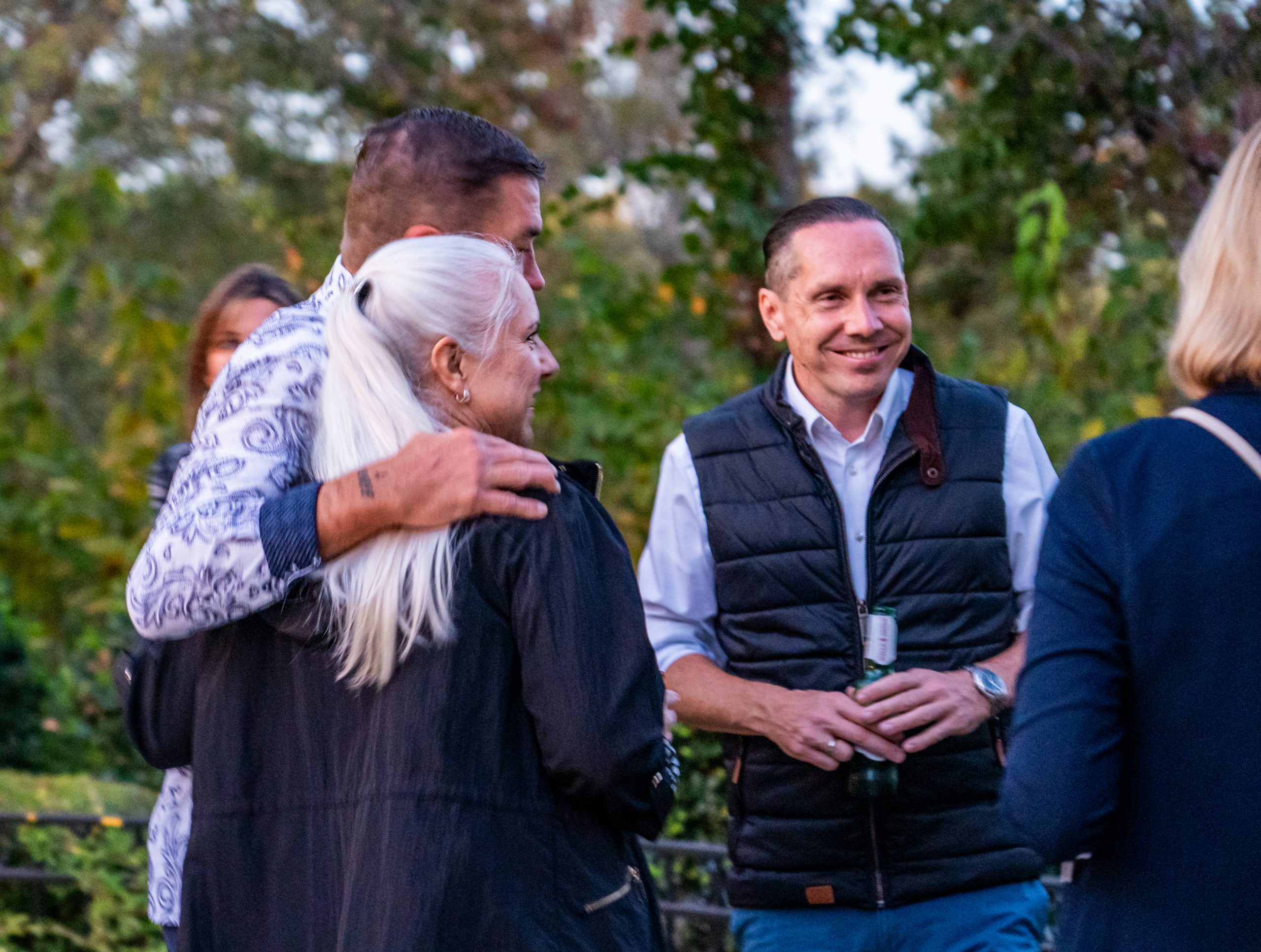 Eine Menschen Gruppe unterhält sich auf einer Feier, ein Mann steht dabei Arm in Arm mit einer Frau