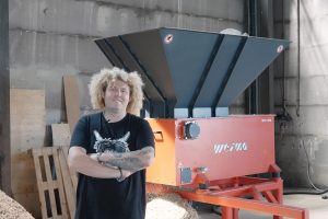A man with blond hair in front of an orange shredder