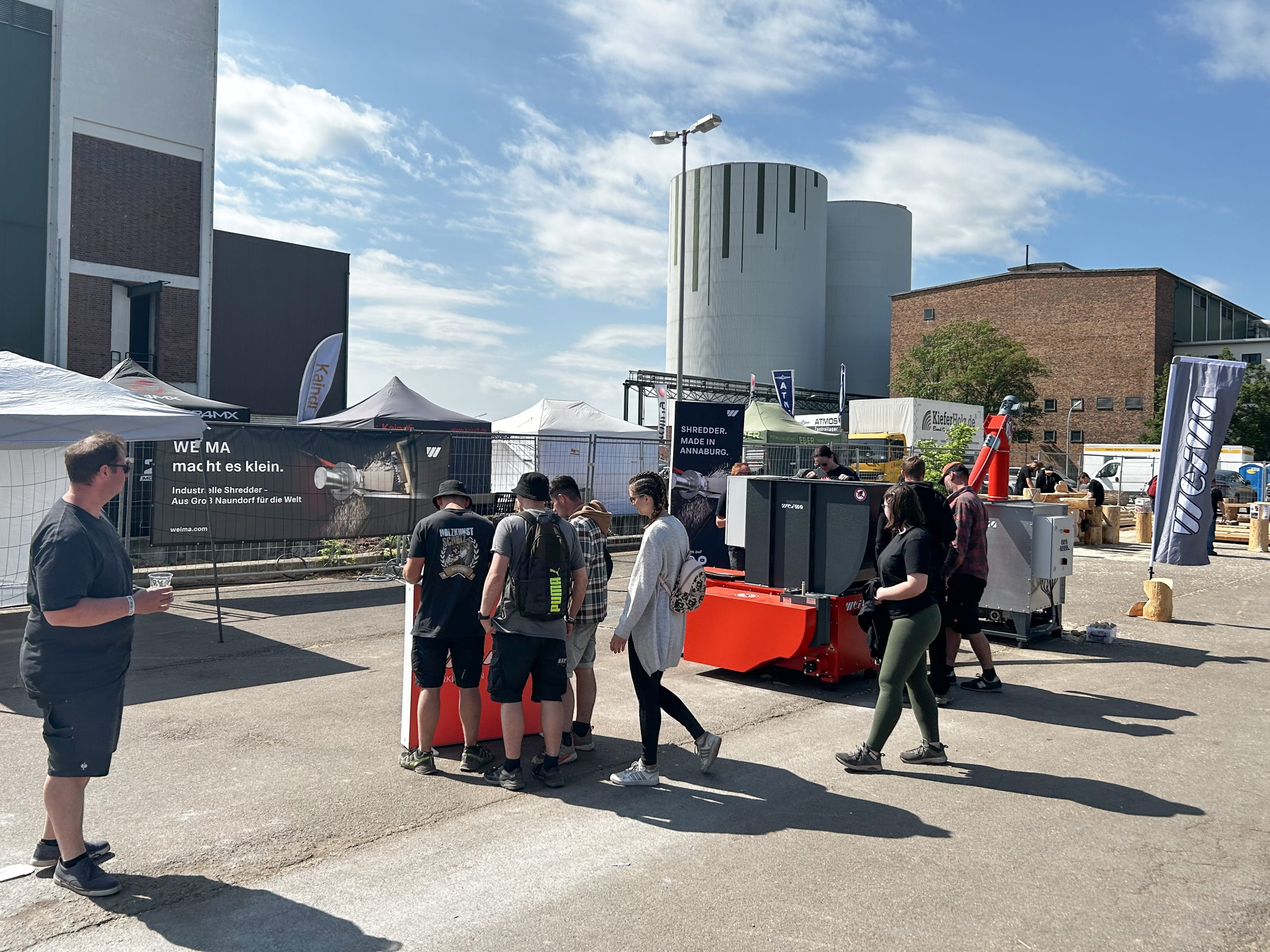 Mehrere Menschen vor einem orangefarbenen Shredder auf einem Industriegelände während eines Festivals