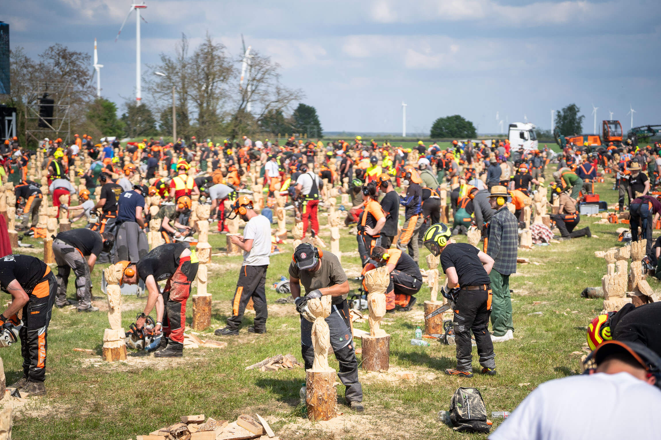 Sehr viele Leute mit Kettensägen die eine Figur aus einem Holzblock schnitzen