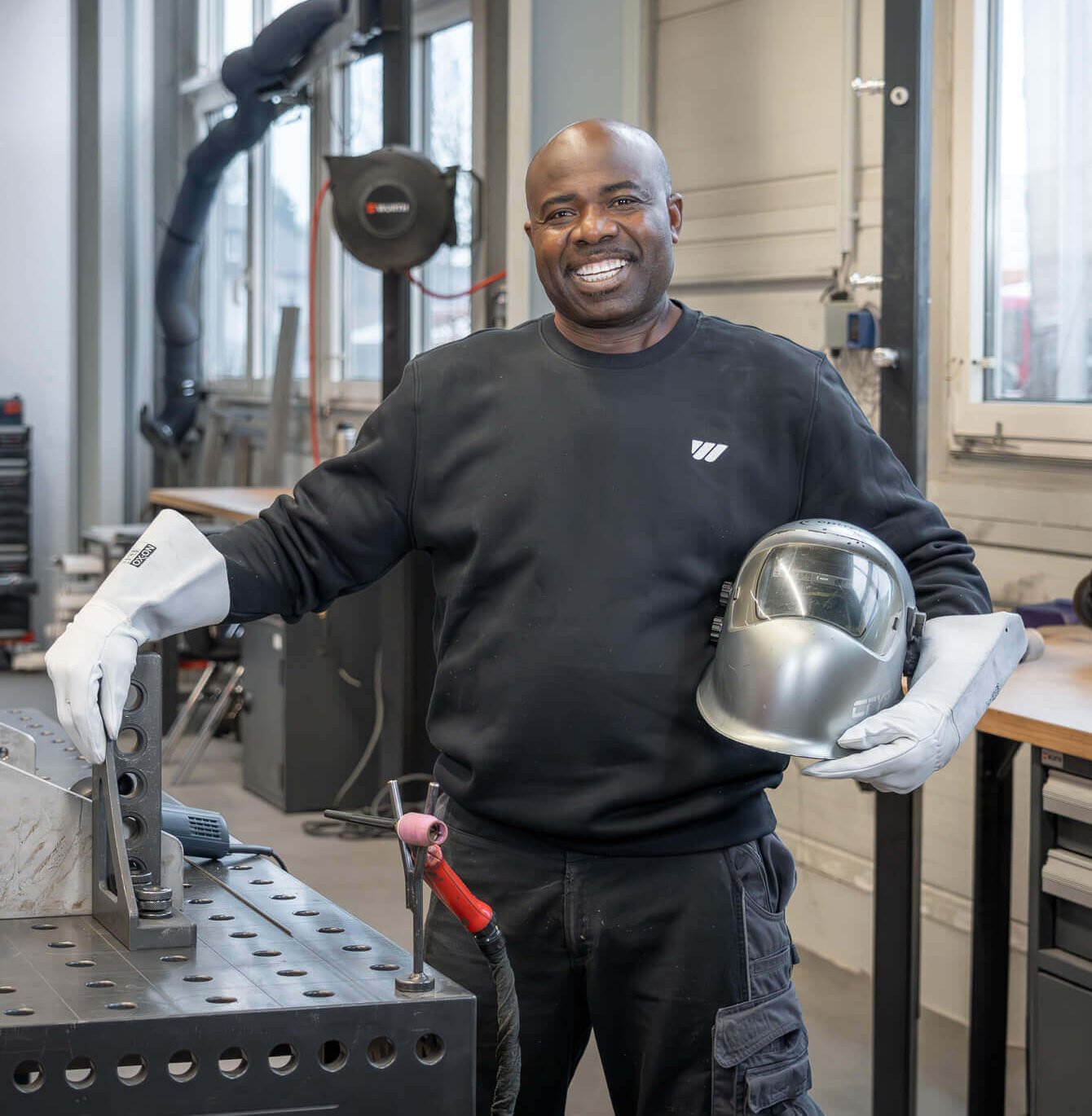 Mitarbeiter mit Schweißhelm bei WEIMA steht lachend am Schweißtisch