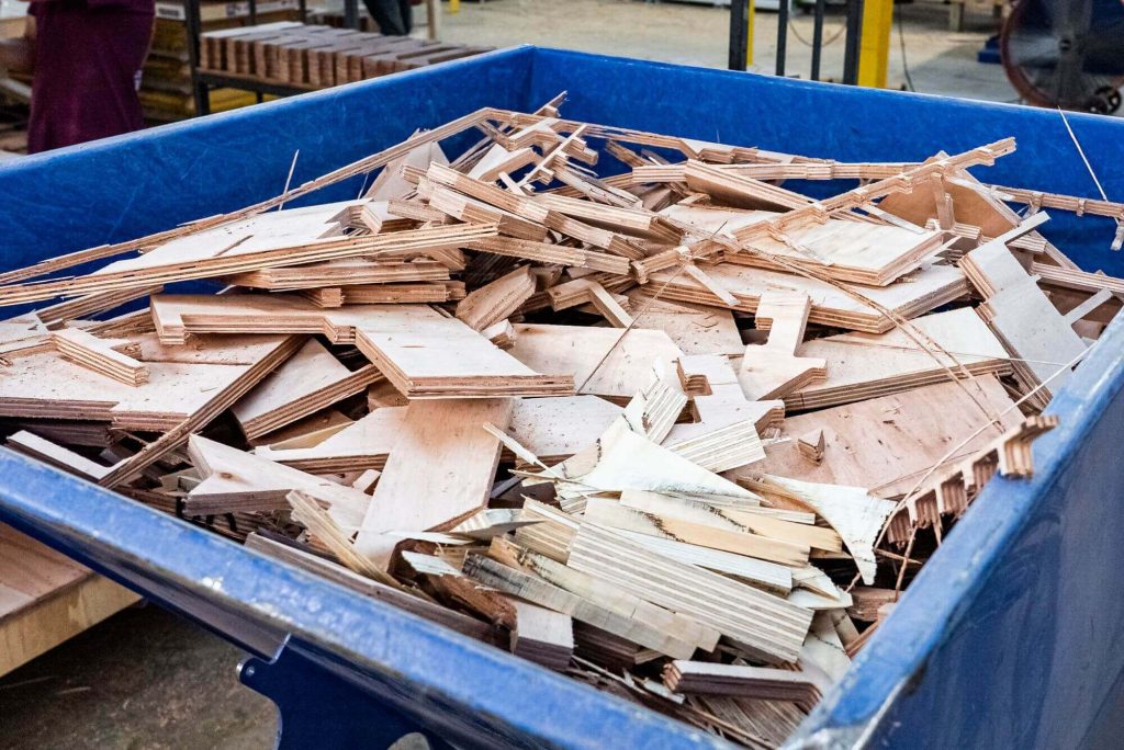 A blue metal wheely bin is filled with plywood scraps.