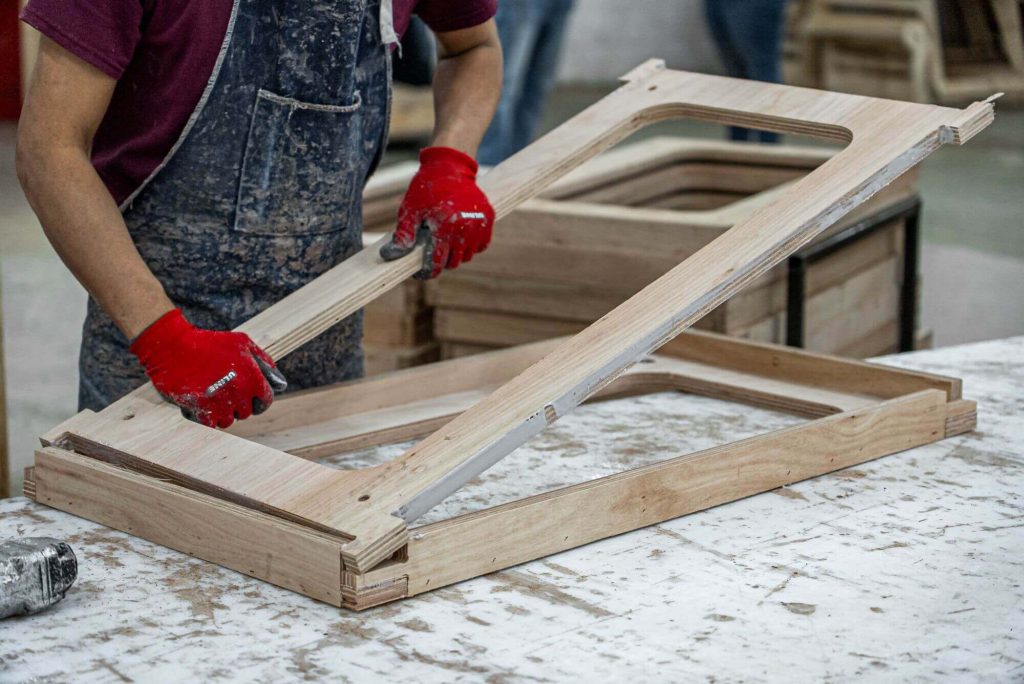 A man wearing red gloves and overalls assembles a piece of furniture on a work table.