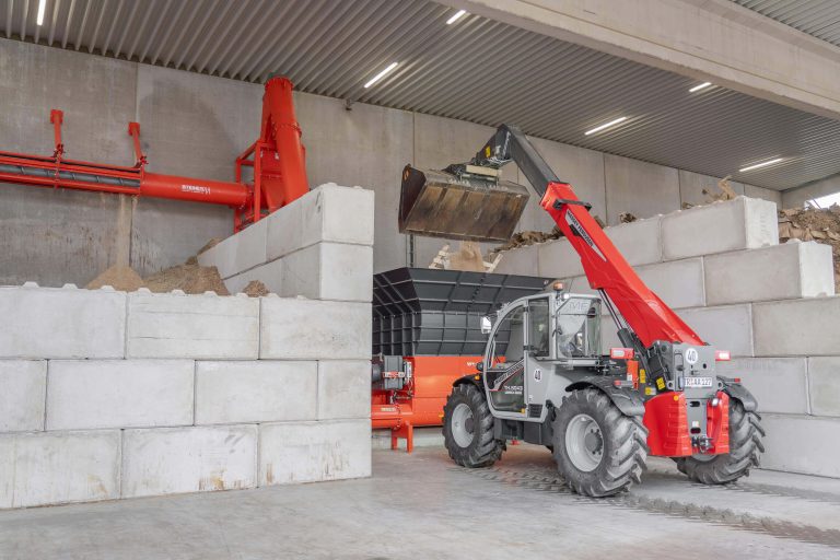 Ein Teleskoplader befördert Holzreste in einen großen Trichter zur Weiterverarbeitung.