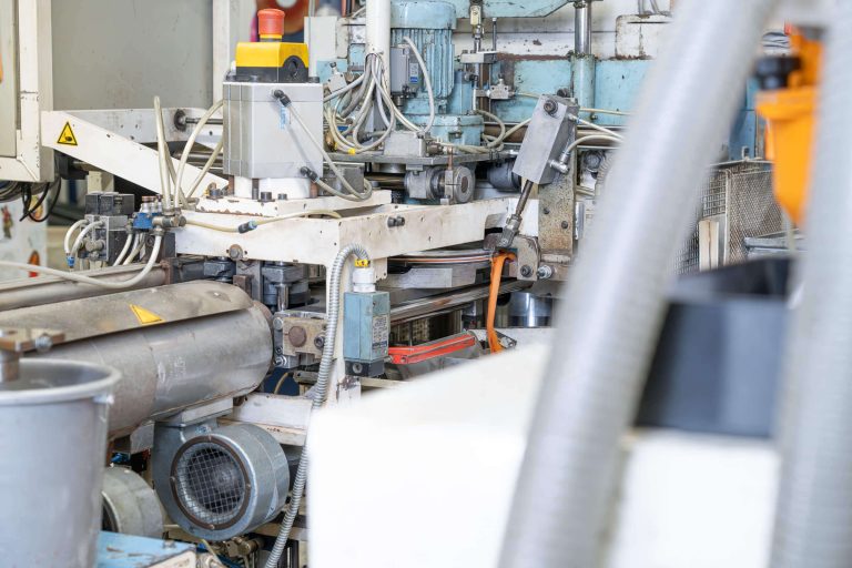 Close-up of a record pressing machine, showing the removal of an orange PVC overhang