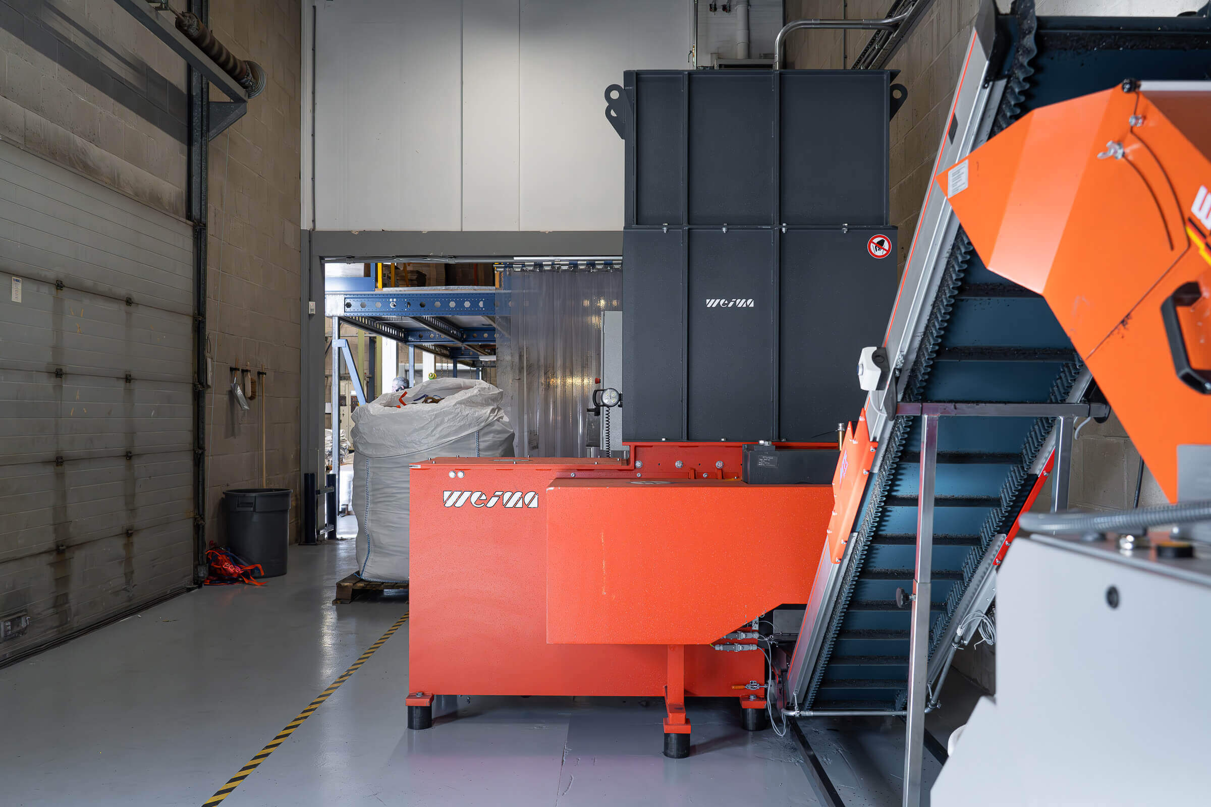 Side view of a WEIMA WLK 4 plastic shredder with electromechanical drive and WEIMA WAP gearbox, to the right a conveyor belt