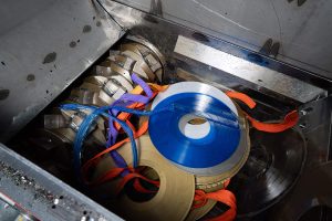 Colorful records lie in the cutting chamber of a shredder in front of the rotor with cutting blades