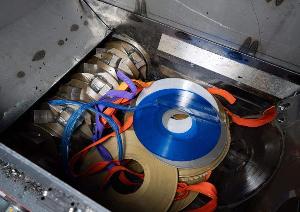 Bunte Schallplatten liegen im Schneidraum eines Shredders vor dem Rotor mit Schneidmessern