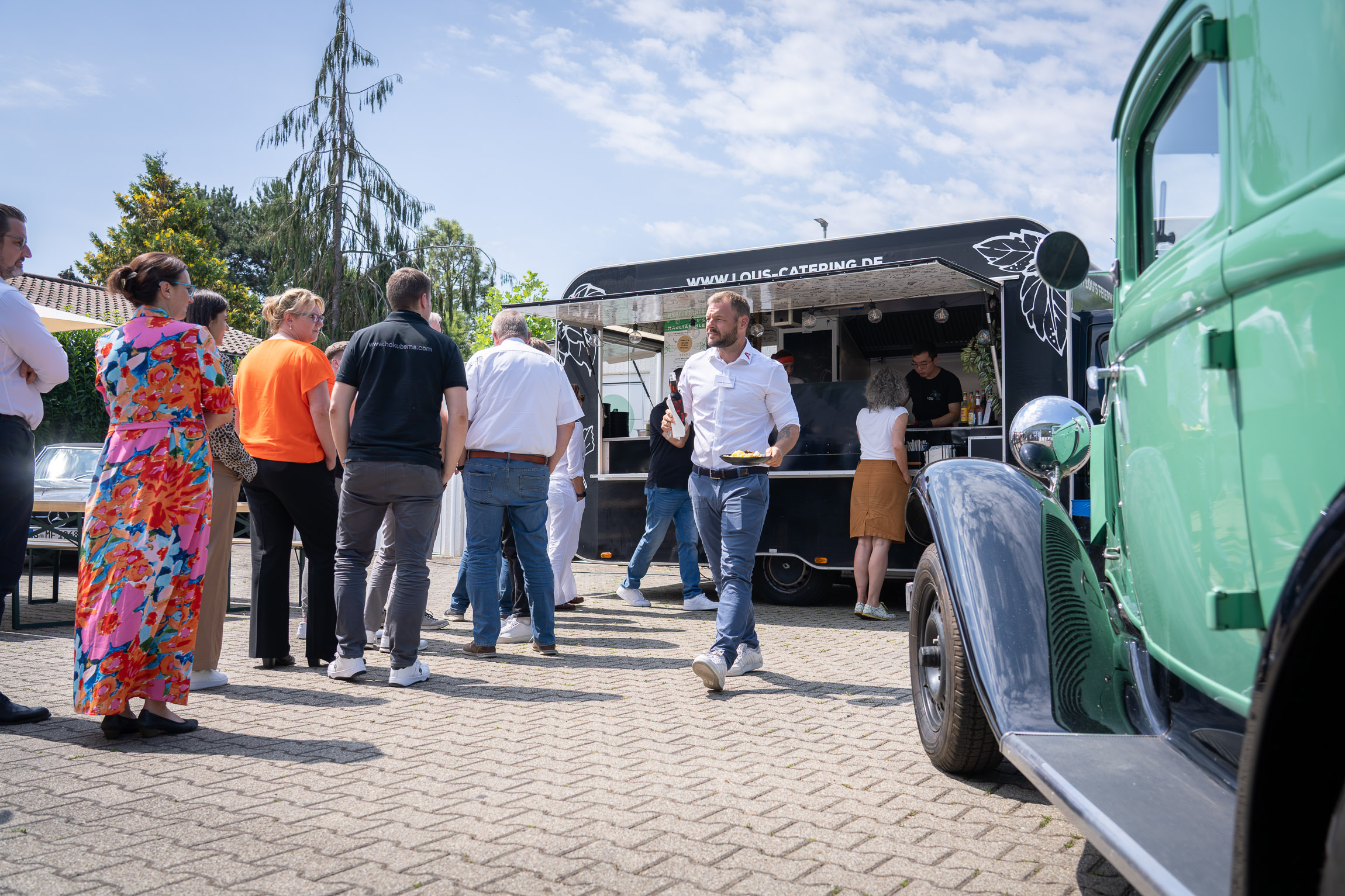 Vor einem Foodtruck stehen Personen bei strahlendem Sonnenschein an für Essen
