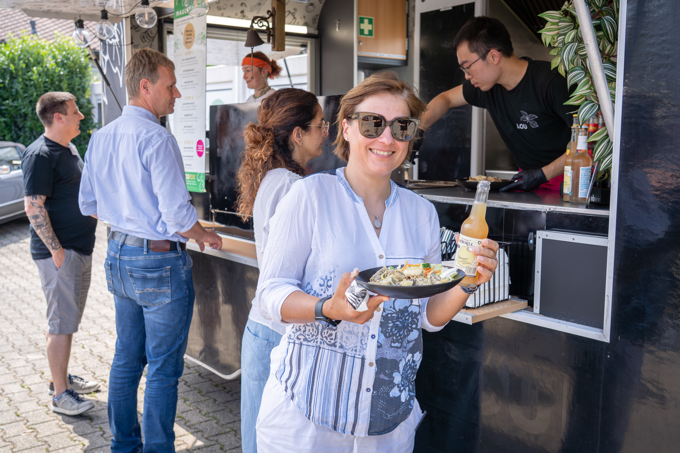 Eine Frau steht vor einem Foodtruck und grinst mit ihrem Teller Maultaschen in die Kamera