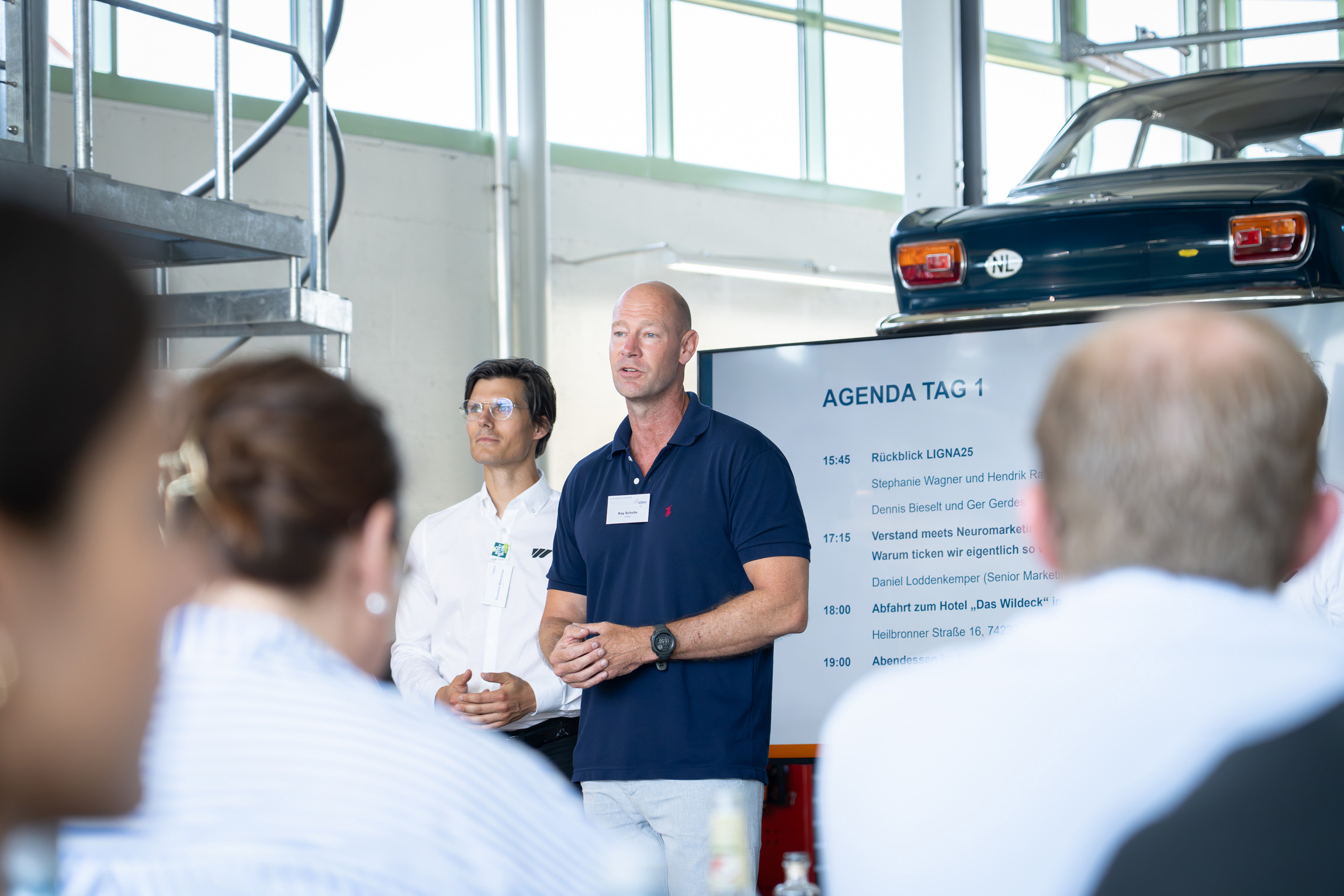 Zwei Mitarbeiter von WEIMA stehen vorne und begrüßen die Gäste