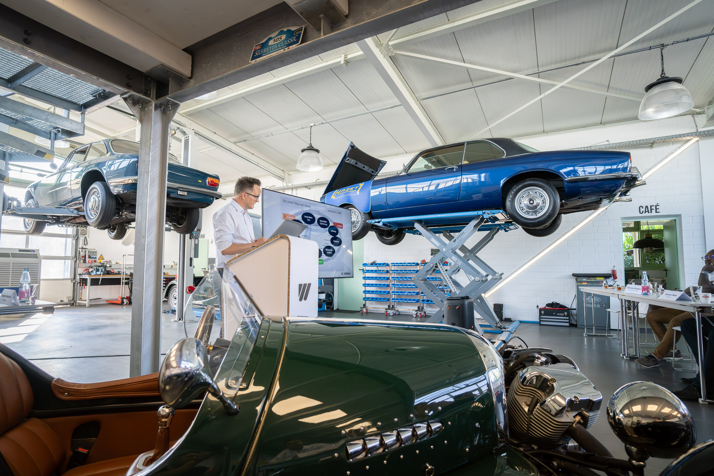 Ein Mann hält einen Vortrag über Neuromarketing, er steht in Mitten von alten Oldtimer der WEIMA Garage