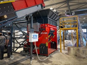 An orange shredder in a warehouse with a conveyor belt and a roll feeder with BOPP film.
