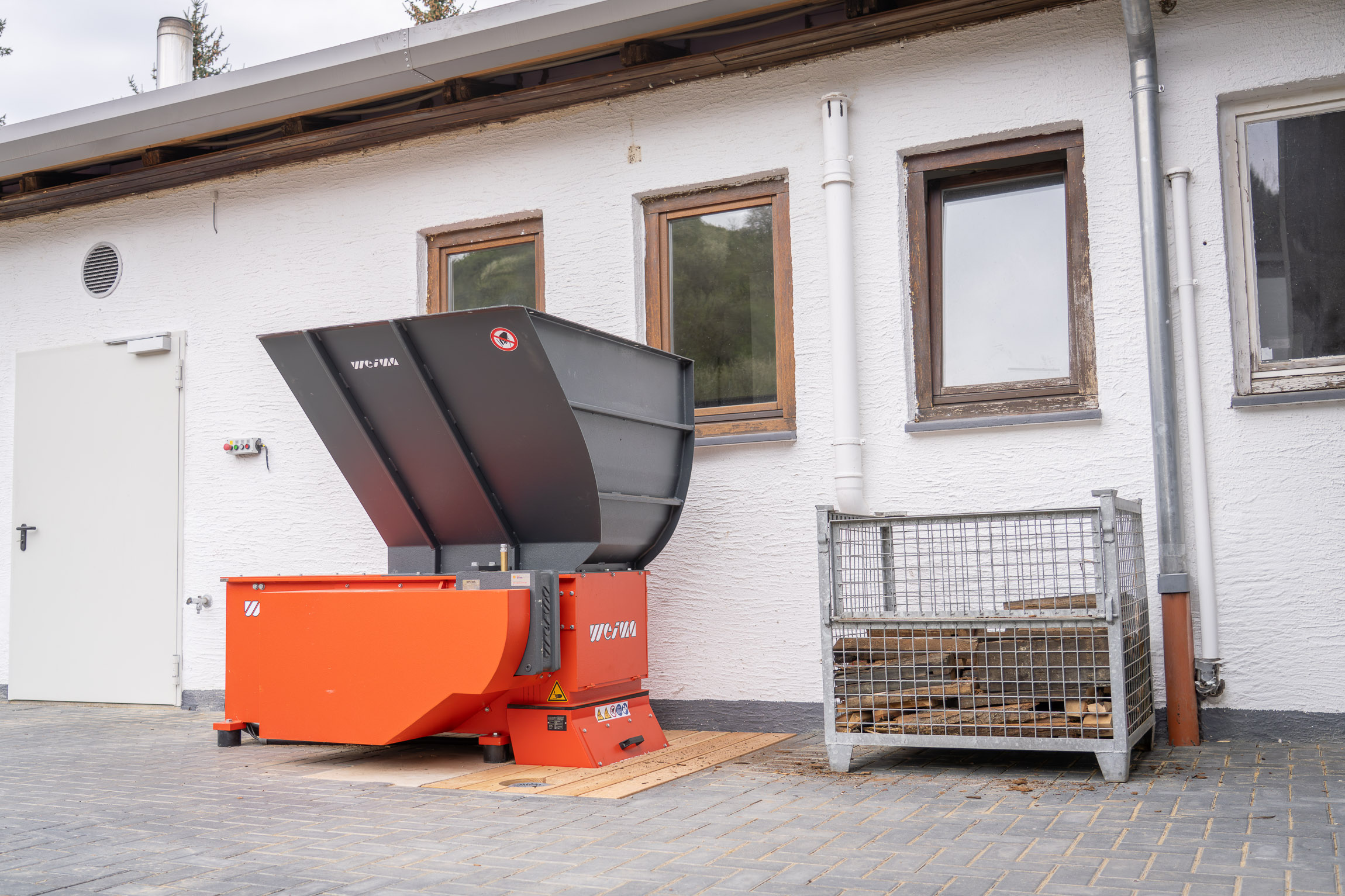 The orange shredder is outside in front of the carpentry shop.
