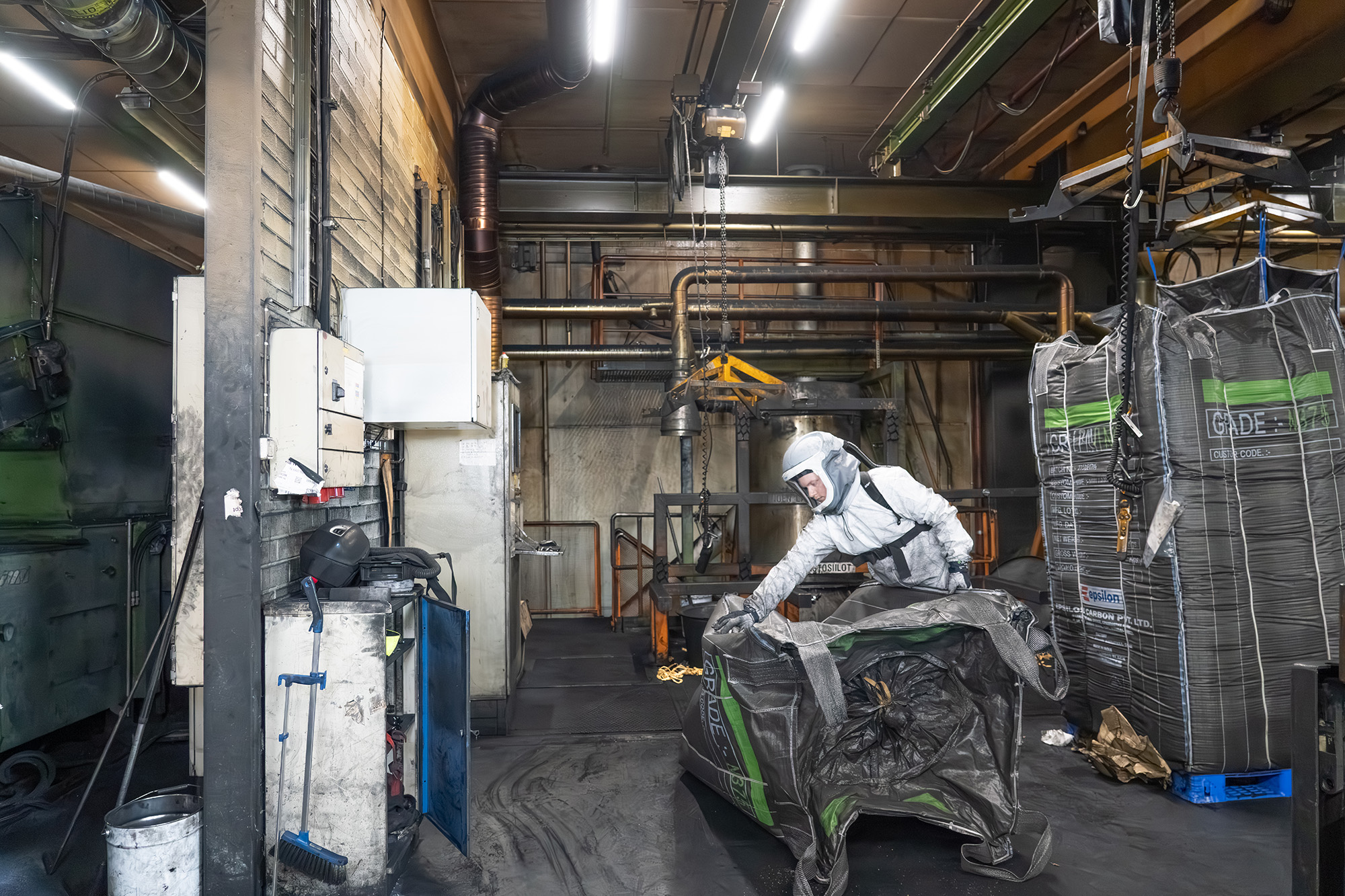 A man in a white protective suit holding an empty black big bag in the hall of a tire manufacturer.