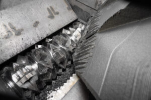 Inside a shredder with a shiny rotor shredding a big piece of black plastic