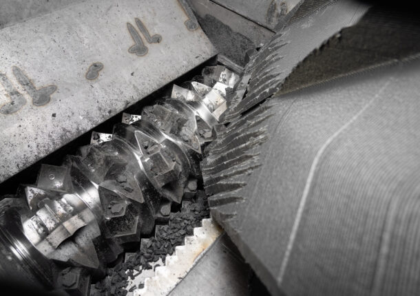 Inside a shredder with a shiny rotor shredding a big piece of black plastic
