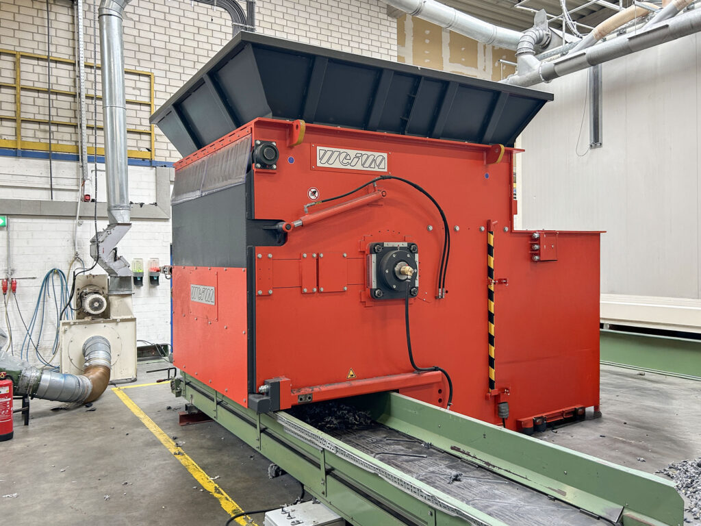 Orange shredder with green conveyor belt in a warehouse