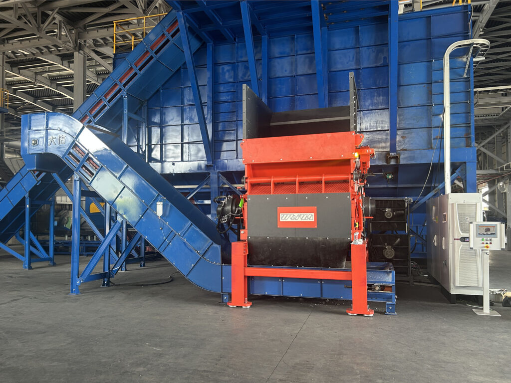 Ein orangefarbener Shredder mit blauen Förderband in einer Lagerhalle