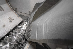 Im Inneren eines Schredders mit einem glänzenden Rotor, der ein großes Stück schwarzen Kunststoff zerkleinert