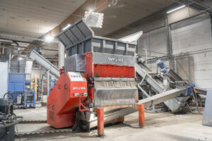 An orange shredder in a warehouse with an attached screw conveyor
