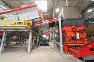 Ein orangener WEIMA PowerLine shredder, verbunden mit einem großen Förderband