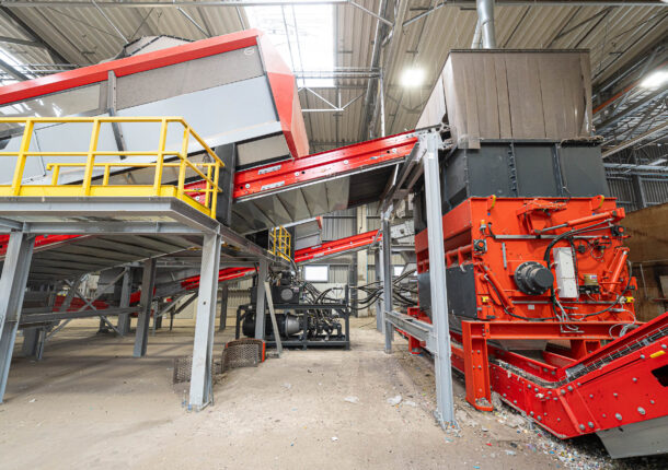 Ein orangener WEIMA PowerLine shredder, verbunden mit einem großen Förderband