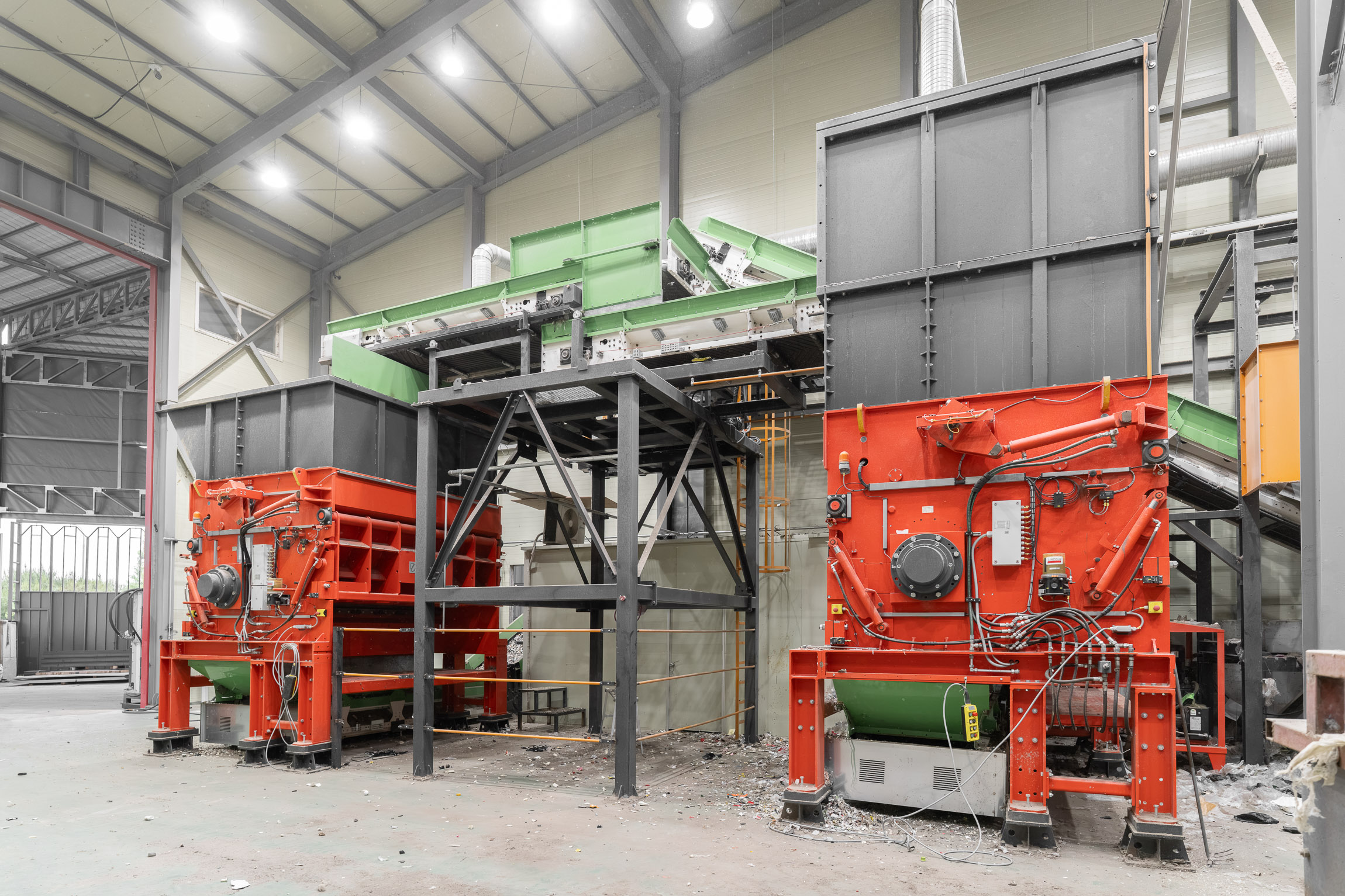 Two large orange shredders being fed waste simultaneously by a conveyor belt