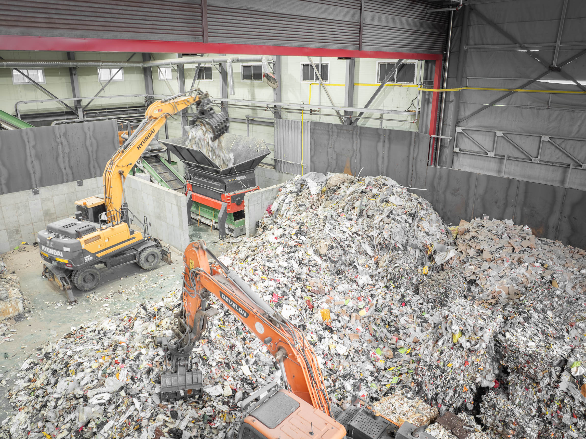 Drone footage of mountains of trash being fed into an orange shredder by two excavators