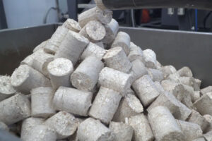 Ein Stapel von runden Holzbriketts die aus einem Austragsrohr kommen
