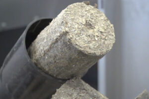 A round straw briquette comes out of a discharge tube